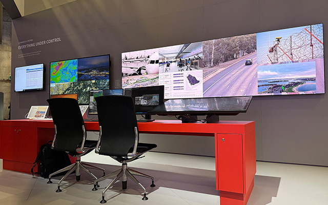 A red desk with two office chairs in from of a bank of screens
