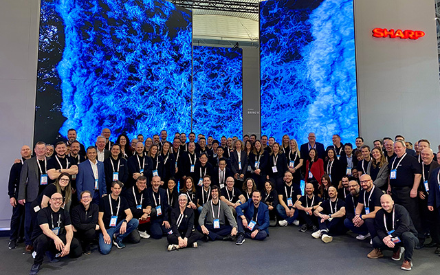 A large group of colleagues gather in front of a LED wall