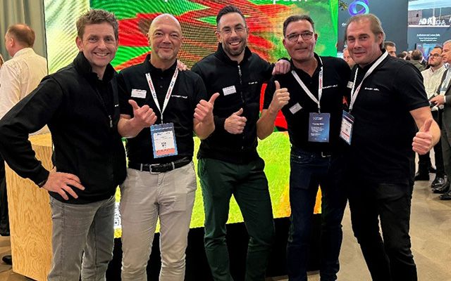 five men in black polo shirts stand smiling and giving the thumbs up